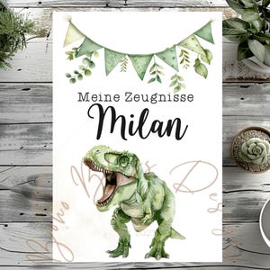 Puede incluir: Impresión blanca con una ilustración de acuarela de un Tyrannosaurus Rex verde con la boca abierta. El texto "Meine Zeugnisse Milan" está encima del dinosaurio, con una guirnalda de banderas y hojas verdes.