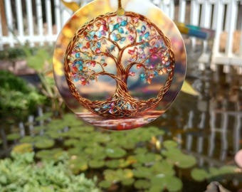 May include: A round, glass ornament with a colorful tree of life design. The tree is made of wire and has many small, colorful beads for leaves. The background is a blurred image of a pond with lily pads.