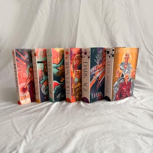 May include: A row of seven hardback books with vibrant covers. Titles visible are "Red Rising," "Golden Son," "Morning Star," "Iron Gold," "Dark Age," and "Light Bringer." The spines show the titles and author's name.