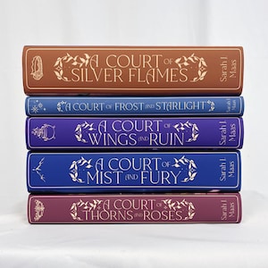 Peut inclure: Une pile de cinq livres reliés de la série "A Court of Thorns and Roses" de Sarah J. Maas. Les livres sont dans des tons de marron, bleu, violet et bordeaux, avec des motifs floraux décoratifs et du texte.
