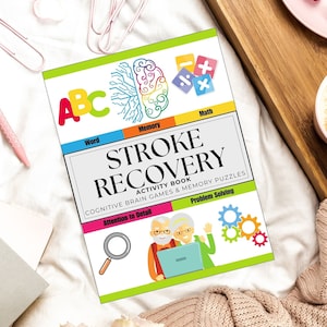 May include: A colorful activity book titled "STROKE RECOVERY" with the subtitle "Cognitive Brain Games & Memory Puzzles." The cover features illustrations of a brain, math symbols, and an elderly couple. Other items include a coffee cup, croissant, and a pink pen.