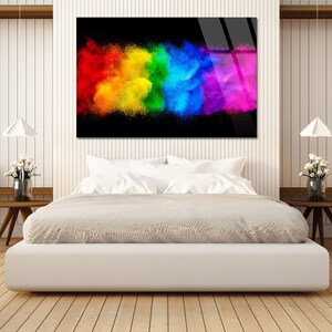 May include: A colorful abstract art print with a rainbow explosion of color on a black background. The print is hanging on a white wall above a white bed with white bedding.