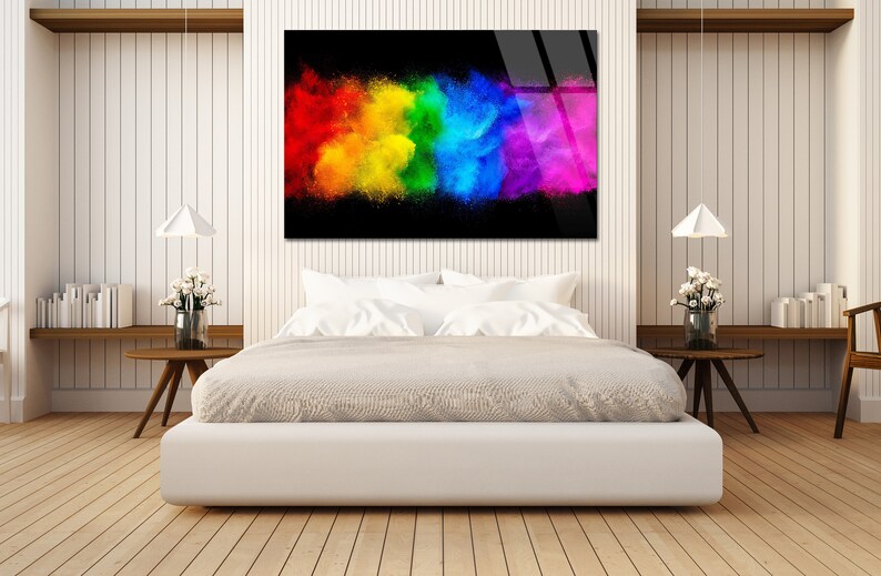 May include: A colorful abstract art print with a rainbow explosion of color on a black background. The print is hanging on a white wall above a white bed with white bedding.