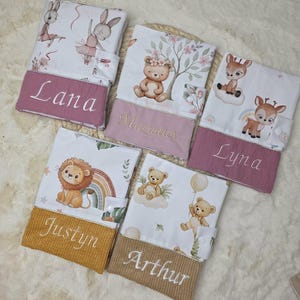 Peut inclure: Cinq protège-carnets de santé rectangulaires en tissu, chacun présentant un motif animalier unique et une section inférieure unie brodée des prénoms Lana, Margaux, Lyna, Justyn ou Arthur en lettres cursives blanches ou dorées.