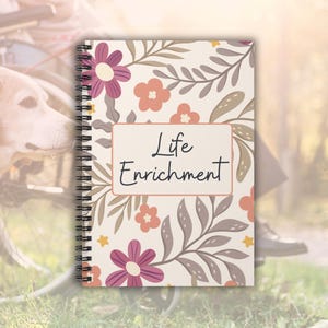 May include: A spiral bound journal with a floral pattern in shades of pink, orange, and gray. The cover features the text "Life Enrichment" in a black font.