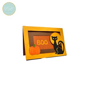 May include: A Halloween-themed card with a pumpkin and a black cat silhouette. The card features the word "BOO" in orange letters. The background is orange and brown, with a yellow frame.