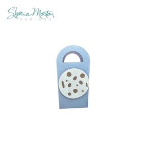 May include: A light blue gift bag with a handle, featuring a white circle with brown spots. The bag has a circular cutout at the top. The text "Sharia Morton DESIGNS" is in the upper left corner.