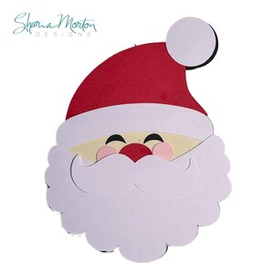 May include: A Santa Claus face cutout with a red hat, white beard, and rosy cheeks. The design includes a white mustache and a small red nose. The text "Sharia Morton DESIGNS" is in the upper left corner.