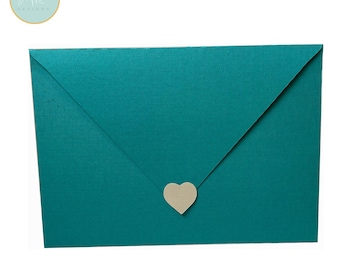 May include: Teal envelope with a heart-shaped closure. The envelope has a textured surface and a triangular flap. The heart closure is a light beige color. The upper left corner has a circular logo with the text "Shane Morton DESIGNS".