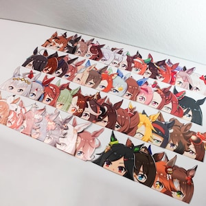 May include: A collection of colorful anime-style character stickers, each featuring a unique design with detailed eyes and hair. The stickers are arranged in rows, showcasing a variety of characters with different color schemes and expressions.
