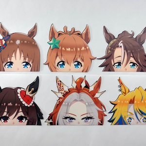 May include: Six anime-style character head cutouts with large eyes and various hair colors, including brown, orange, and yellow. Each cutout features a unique hairstyle and accessories, such as bows and stars.