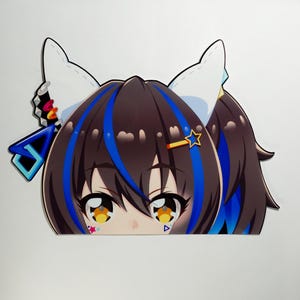 May include: A die-cut sticker featuring a cartoon anime character with brown hair, blue highlights, and cat ears. The character has large, expressive eyes with yellow and orange details, and a star-shaped hair accessory.