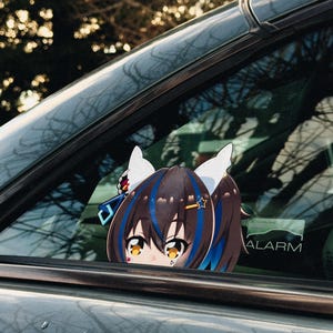 May include: A car window decal featuring an anime-style character with brown hair, blue highlights, and white ears. The decal is visible through the car window, with the word "ALARM" visible on the window.