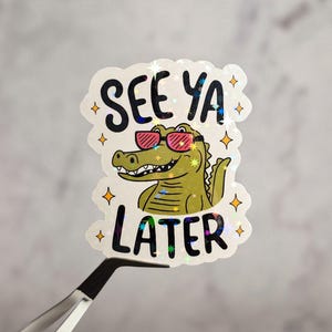 May include: A white sticker with a green alligator wearing sunglasses and the text "See ya later" in black letters.