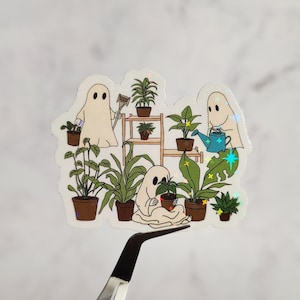 May include: A sticker featuring three white ghosts tending to a collection of potted plants. The ghosts are depicted with simple, cartoon-like features. One ghost is watering a plant, another is holding a gardening tool, and the third is holding a potted plant. The sticker has a holographic finish.