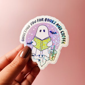 May include: A holographic sticker with a ghost reading a book and holding a cup of iced coffee. The sticker says "Ghosting you for books and coffee".