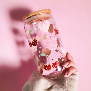 May include: A clear glass tumbler with a bamboo lid, decorated with pink cherries, hearts, and bows. The tumbler has a straw and is held against a pink background. The design includes red, pink, and brown elements.