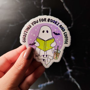 May include: A holographic sticker with a ghost reading a book and holding a cup of iced coffee. The sticker says "Ghosting you for books and coffee".