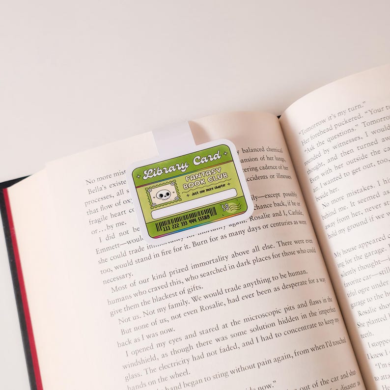May include: A green and black library card with a skull and crossbones graphic. The card says "Fantasy Book Club" and "Just one more chapter".