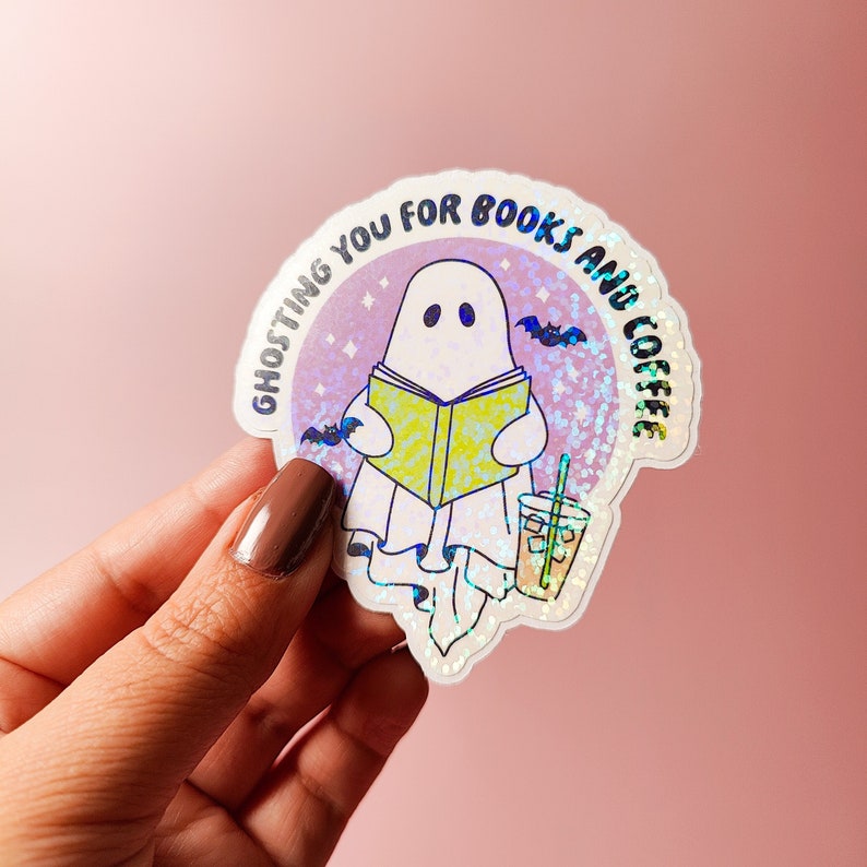 May include: A holographic sticker with a ghost reading a book and holding a cup of iced coffee. The sticker says "Ghosting you for books and coffee".