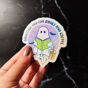 May include: A holographic sticker with a ghost reading a book and holding a cup of coffee. The sticker says "Ghosting you for books and coffee."