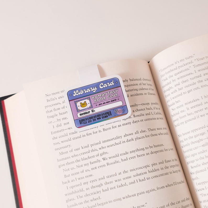 May include: A pink and purple library card with a cartoon frog and the text "Romantasy Book Club". The card has a barcode and the text "Member ID: 111 222 333 444 55556".