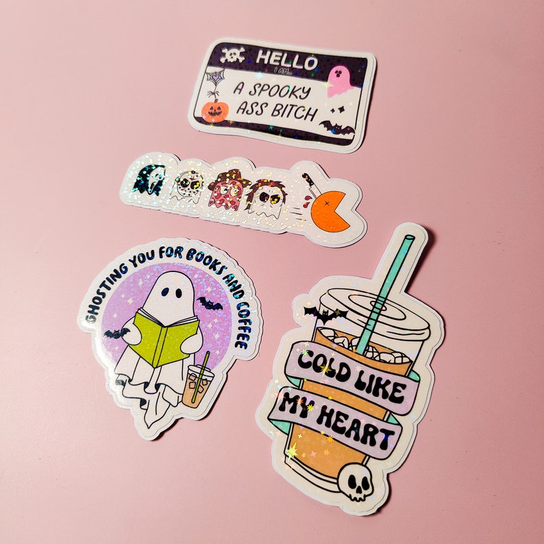 May include: Four holographic stickers with spooky Halloween themes. The first sticker says "Hello I am a spooky ass bitch" with a pumpkin and bats. The second sticker has a line of ghosts and a Pac-Man. The third sticker says "Ghosting you for books and coffee" with a ghost reading a book. The fourth sticker says "Cold like my heart" with a cup of iced coffee and a skull.
