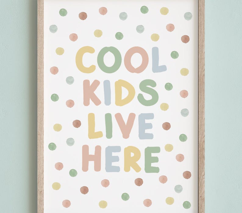 May include: A framed print with the words "COOL KIDS LIVE HERE" in colorful, playful lettering. The background is white with scattered polka dots in pastel shades of pink, yellow, green, and brown. The frame is a light wood color.