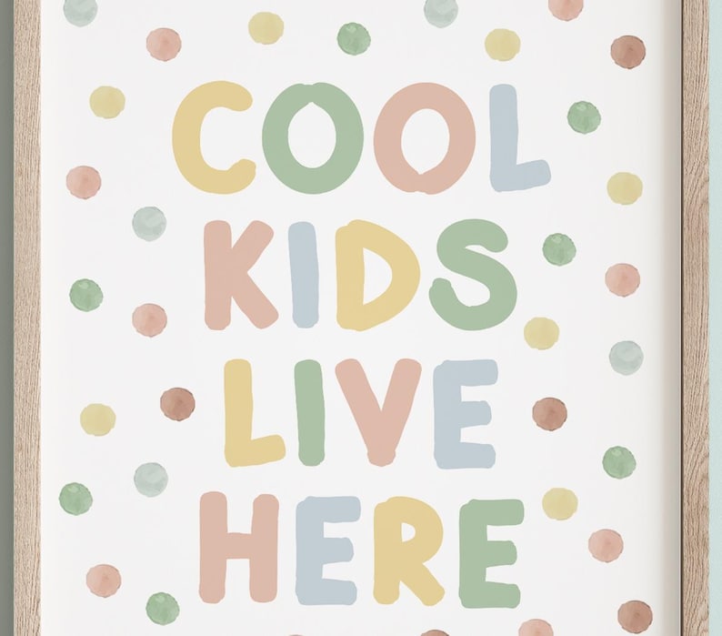 May include: A framed print with the words "COOL KIDS LIVE HERE" in colorful, rounded letters. The text is surrounded by watercolor-style polka dots in pastel shades of yellow, green, pink, and blue. The frame is a light wood color.