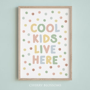 May include: A framed art print with the words "COOL KIDS LIVE HERE" in pastel colors. The print is decorated with colorful polka dots and has a light wood frame. The text is in a playful font, perfect for a child's room.