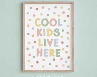 May include: A framed art print with the words "COOL KIDS LIVE HERE" in pastel colors. The print is decorated with colorful polka dots and has a light wood frame. The text is in a playful font, perfect for a child's room.