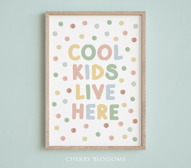 May include: A framed art print with the words "COOL KIDS LIVE HERE" in pastel colors. The print is decorated with colorful polka dots and has a light wood frame. The text is in a playful font, perfect for a child's room.