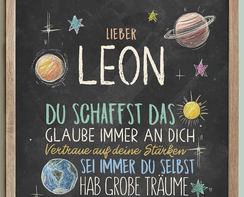 May include: A black chalkboard with white chalk writing. The text says "Lieber Leon", "Du schaffst das", "Glaube immer an dich", "Vertraue auf deine St&auml;rken", "Sei immer du selbst", and "Hab gro&szlig;e Tr&auml;ume". The chalkboard is decorated with drawings of stars, planets, and a sun.