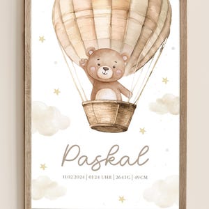 May include: Watercolor illustration of a teddy bear in a hot air balloon. The bear is waving from a wicker basket. The background is white with clouds and stars. The name "Paskal" is written below the balloon.
