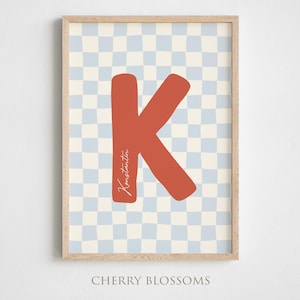 Könnte beinhalten: Gerahmter Kunstdruck mit einem großen, rostfarbenen Buchstaben "K" und dem Namen "Konstantin" in Schreibschrift. Der Hintergrund ist ein hellblaues und cremefarbenes Schachbrettmuster. Die Worte "CHERRY BLOSSOMS" stehen unten.