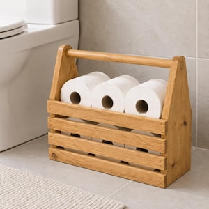May include: A light brown wooden caddy with a handle, designed to hold multiple rolls of white toilet paper. The structure features horizontal slats and an open top, providing a storage solution for bathroom essentials in a rectangular frame.