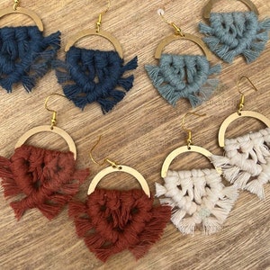May include: A set of six pairs of handmade macrame earrings with gold hoops. The earrings are made with a variety of colours, including navy blue, light blue, cream, and rust.