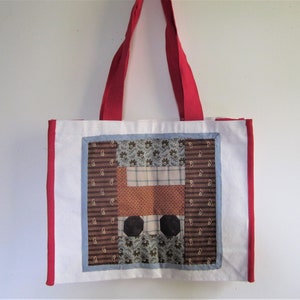 May include: White canvas tote bag with red handles and a patchwork design in the center. The patchwork design features various shades of brown, blue, and white fabrics.