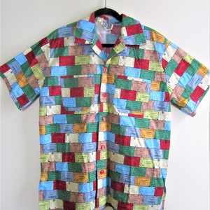 May include: A short-sleeved button-down shirt with a colorful pattern of vintage ticket stubs. The shirt has a red button closure and a pocket on the left side.