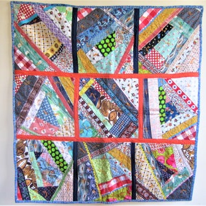 May include: A colorful patchwork quilt with a variety of fabrics and patterns, including floral, geometric, and plaid. The quilt is made up of squares and rectangles, and the seams are visible. The quilt is bordered in blue fabric.