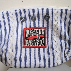 May include: A white and blue striped fabric pouch with a white scalloped trim. The pouch has three black buttons and a red and white patch that says "Western Pacific Feather River Route".