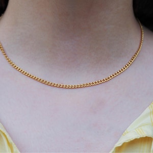 K&ouml;nnte beinhalten: Eine goldfarbene Panzerkettenhalskette. Die Halskette wird um den Hals getragen. Die Kette hat ein gleichm&auml;&szlig;iges, verbundenes Design. Die Person tr&auml;gt ein gelbes kariertes Hemd. Die Kette ist ca. 40 cm lang.