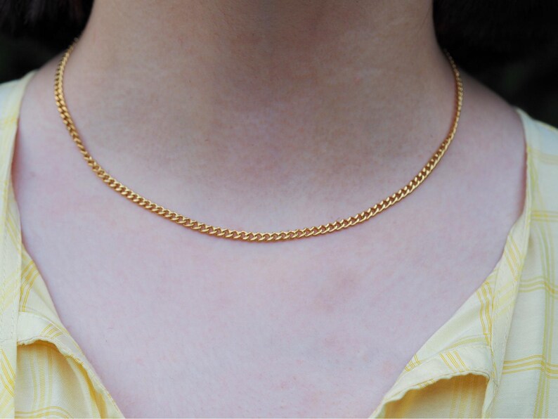K&ouml;nnte beinhalten: Eine goldfarbene Panzerkettenhalskette. Die Halskette wird um den Hals getragen. Die Kette hat ein gleichm&auml;&szlig;iges, verbundenes Design. Die Person tr&auml;gt ein gelbes kariertes Hemd. Die Kette ist ca. 40 cm lang.