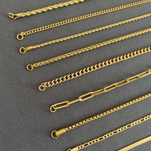 May include: A collection of gold-colored necklaces with various chain styles, including rope, curb, and paperclip designs. Each necklace has a clasp at the end. The chains are displayed on a gray surface.