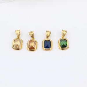 May include: Four gold-coloured pendant necklaces with rectangular gemstones in yellow, orange, blue, and green. Each pendant has a gold bail for a chain. The pendants are displayed on a white background.