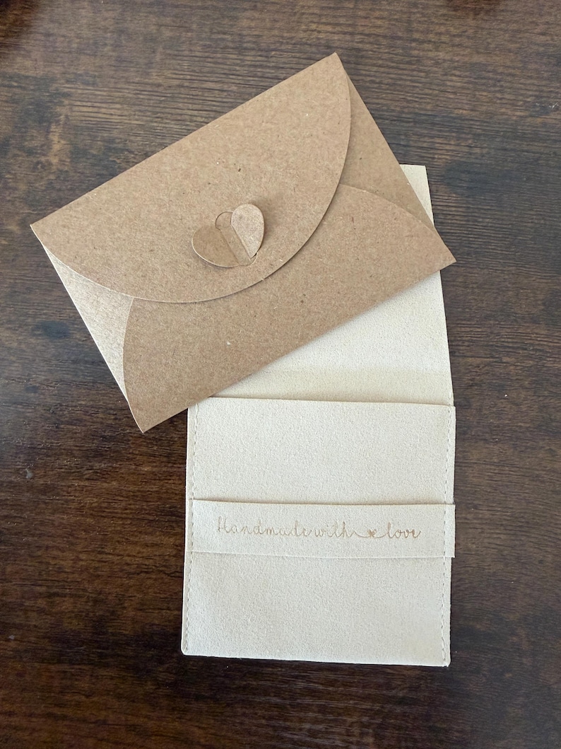 K&ouml;nnte beinhalten: Ein hellbeige Kartenhalter mit passendem Umschlag. Der Umschlag hat einen herzf&ouml;rmigen Verschluss. Auf dem Kartenhalter steht "Handmade with love".