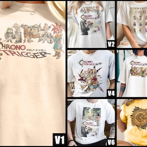 May include: A light beige t-shirt featuring the text "CHRONO TRIGGER" in a circular design, with Japanese text below. The shirt displays a colorful graphic of characters from the video game. The design includes a clock-like element.