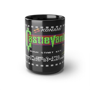 May include: Black ceramic mug with a green and purple Castlevania video game graphic. The text "KONAMI" and "PUSH START KEY" are also on the mug.
