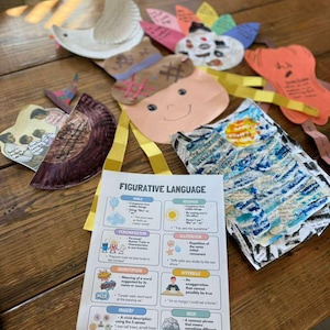 May include: A collection of colorful paper crafts and a printed sheet about figurative language sit on a wooden table. The crafts include a dove, a turkey, and other whimsical figures. The sheet defines literary terms like simile and metaphor.