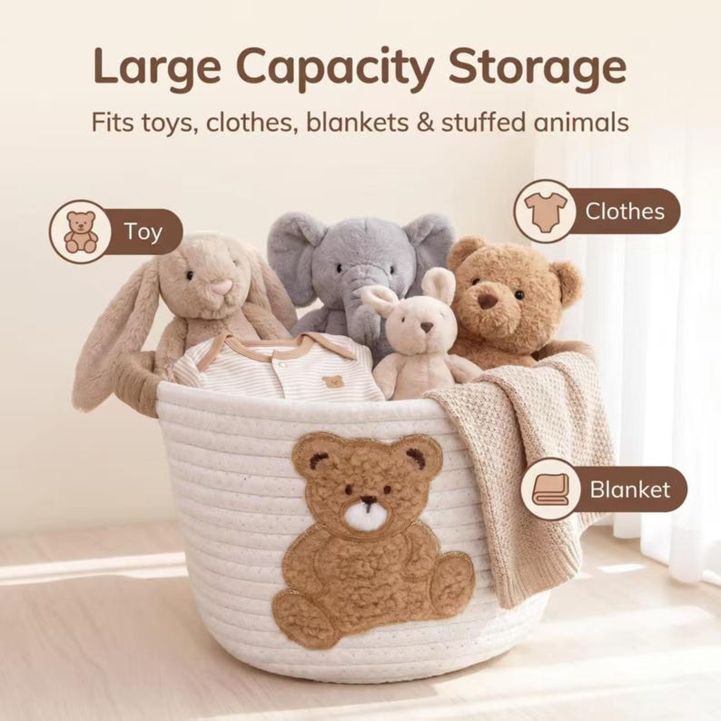 Pode incluir: Uma cesta de armazenamento branca tecida com uma aplica&ccedil;&atilde;o de urso de pel&uacute;cia marrom, cheia de bichos de pel&uacute;cia, um cobertor e roupas de beb&ecirc;. O texto "Large Capacity Storage" est&aacute; no topo.
